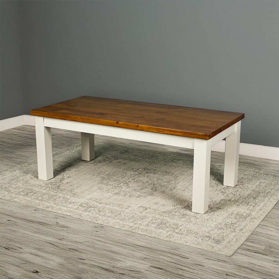 The Alton Mid Size Coffee Table on a rug. There is a free standing potted plant in the back.