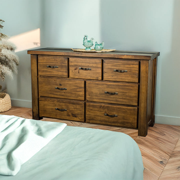 The front of the Botanica Large Seven Drawer Lowboy. There are two blue glass ornaments on top of a rattan leaf.