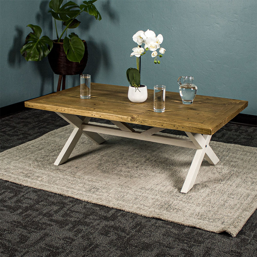 Front view of the Byron Recycled Pine Coffee Table. There are two glasses of water and a pitcher of water on top, as well as a small pot of white flowers.