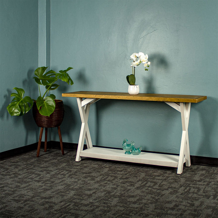 Front view of the Byron Recycled Pine Console Table. There is a standing potted plant next to it, a potted flower on top and two blue glass ornaments on the lower shelf.