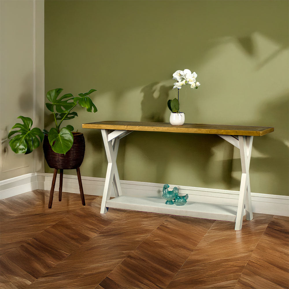 Front view of the Byron Recycled Pine Console Table. There is a standing potted plant next to it, a potted flower on top and two blue glass ornaments on the lower shelf.