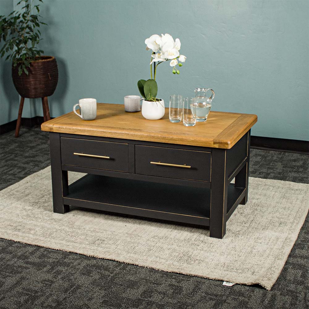 The front of the Cascais 2 Drawer Coffee Table. There is a pot of white flowers on top, two coffee mugs, a pitcher of water and two glasses on top.