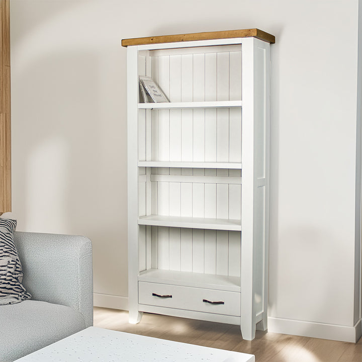 The front of the Felixstowe Large Pine Bookcase. There are two DVDs on the top shelf, and a free standing potted plant next to the bookshelf.