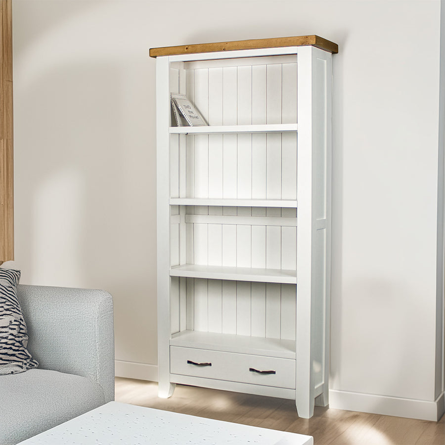 The front of the Felixstowe Large Pine Bookcase. There are two DVDs on the top shelf, and a free standing potted plant next to the bookshelf.