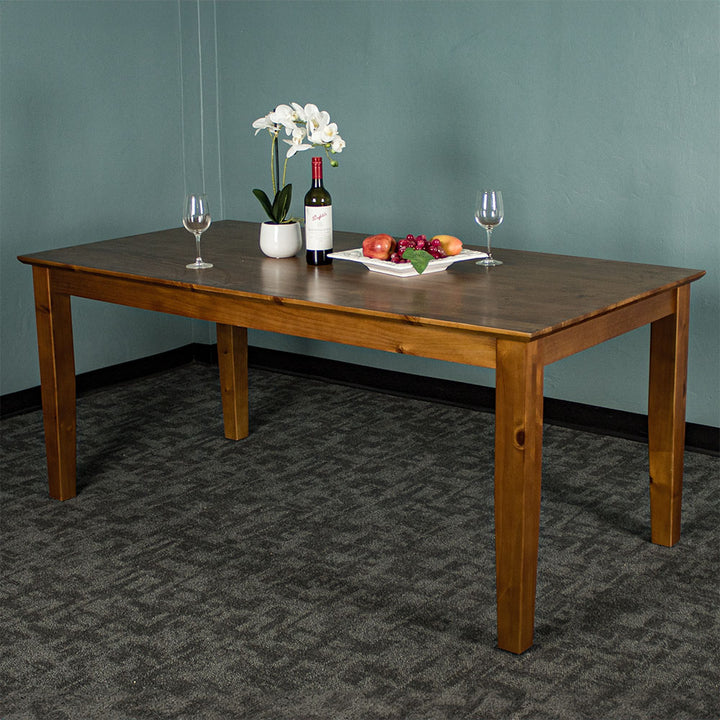 The front of the Hamilton Dining Table with Rimu Finish (1.8m). There are two wine glasses, a pot of white flowers, a fruit platter and a bottle on top of the table.