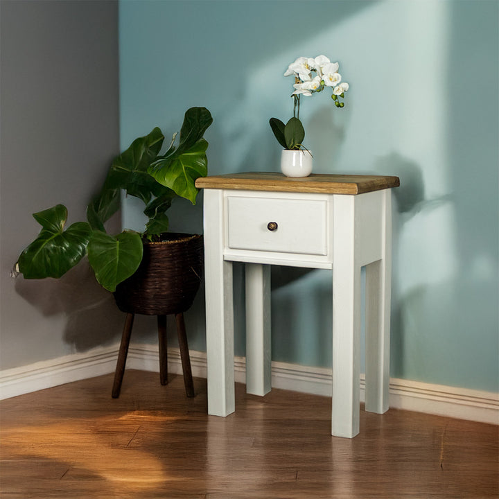 The front of the Loire Oak Console Table. There is a pot of white flowers on top and a free standing potted plant to the left.