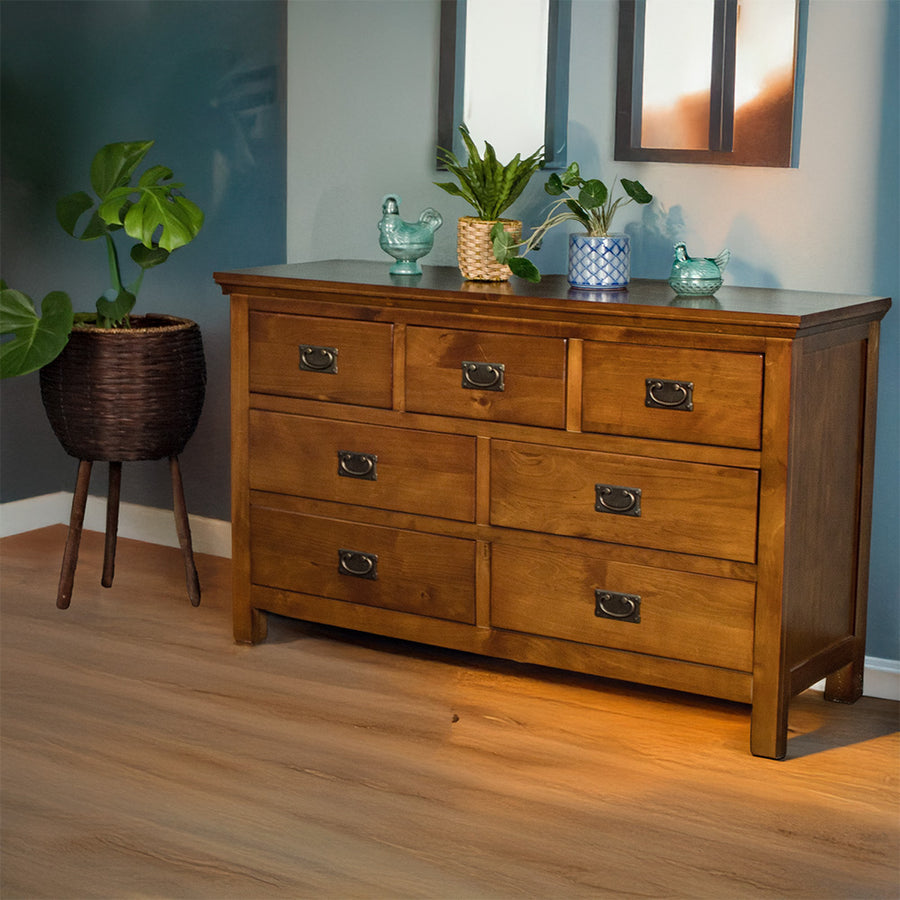 The front of the Montreal 7 Drawer Pine Lowboy. There are two blue glass ornaments on top with two potted plants in between. There is a free standing potted plant next to the lowboy.