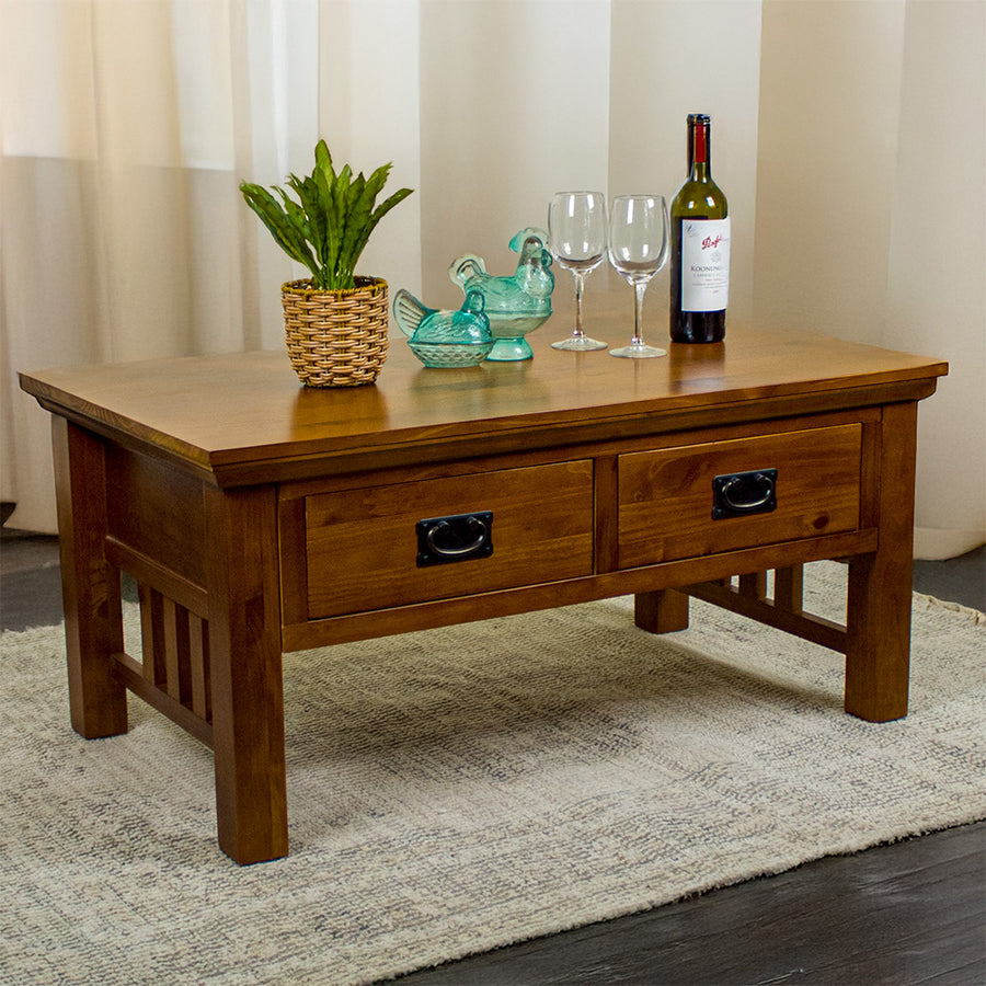 The front of the Montreal Coffee Table with 2 Drawers. There is a potted plant, two blue glass ornaments, two wine glasses, and a bottle of wine on top.