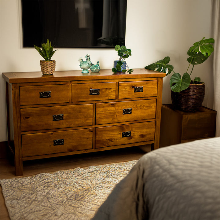 The front of the New Quebec 7 Drawer Lowboy. There are two potted plants on top with two blue glass ornaments in between. There is a free standing potted plant next to the lowboy.