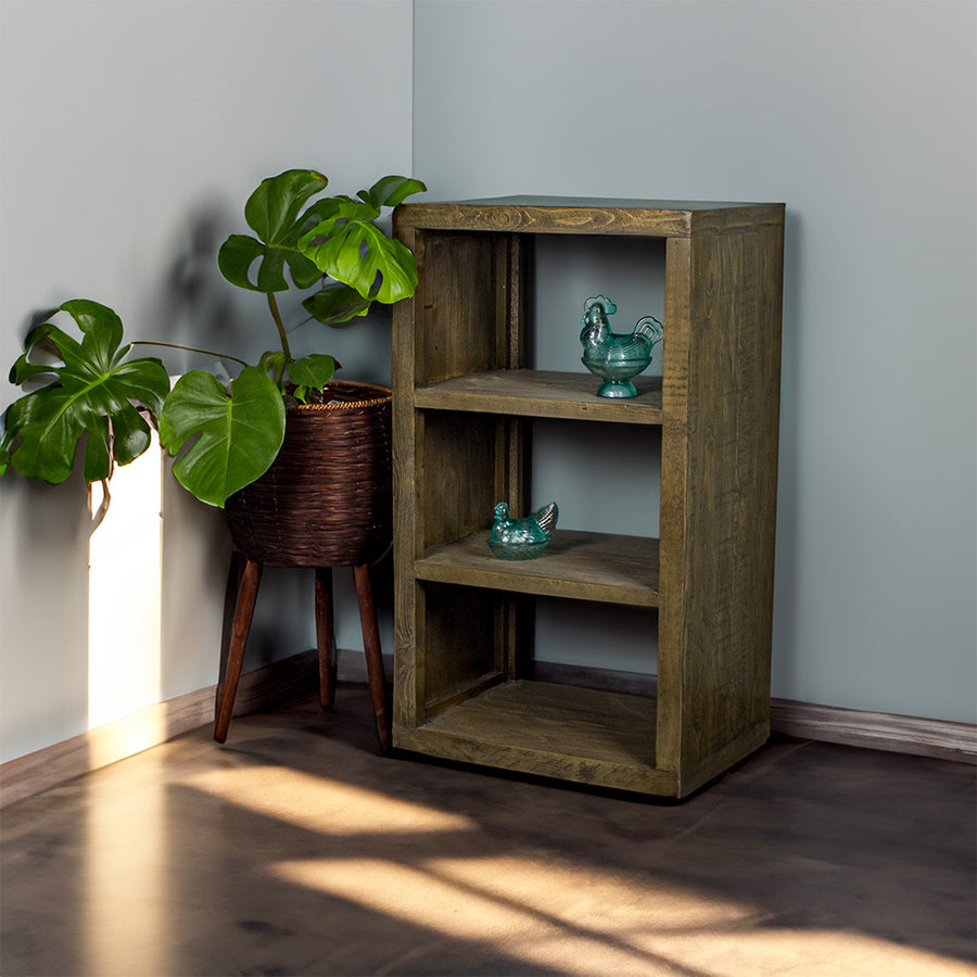 The Stonemill Recycled Pine Cube Shelf, with three shelves. There are two blue glass ornaments, one on the middle and one on the top shelf. There is a tall free standing potted plant next to the cube shelf.