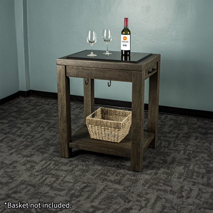 Front view of the Stonemill Recycled Pine Granite Workbench. There are two glasses and a bottle on the granite top, and a woven basket on the lower shelf.