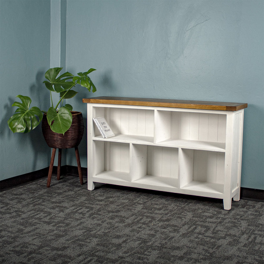 Front view of the Tuscan Recycled Pine Low Bookcase. There is a standing potted plant to the left of it, and two DVD cases on the top left shelf.