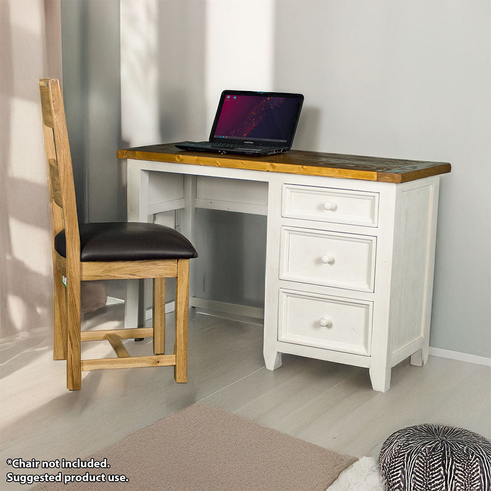 The front of the Tuscan Recycled Pine Small Desk. There is a laptop on top and an oak upholstered dining chair in front. There is a free standing potted plant next to it.