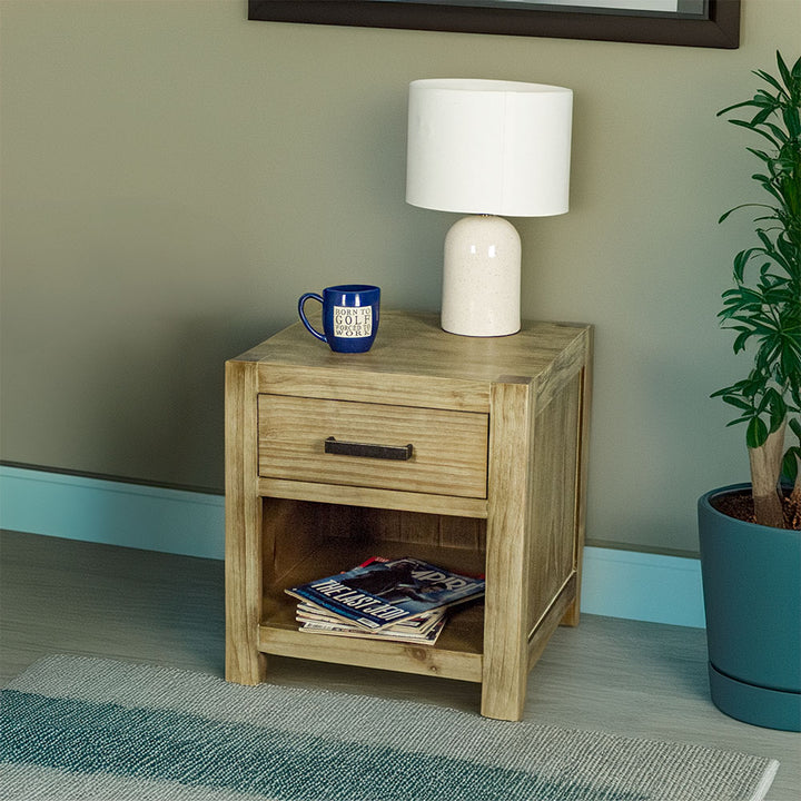 The front of the Vancouver 1 Drawer Lamp Table with a lamp and a coffee mug on top. There is a pile of magazines in the shelf underneath.