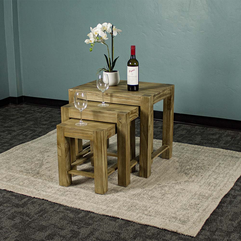 The front of the Vancouver Pine Nesting Tables. There are two wine glasses, a bottle of wine and a pot of white flowers on top of the tables.