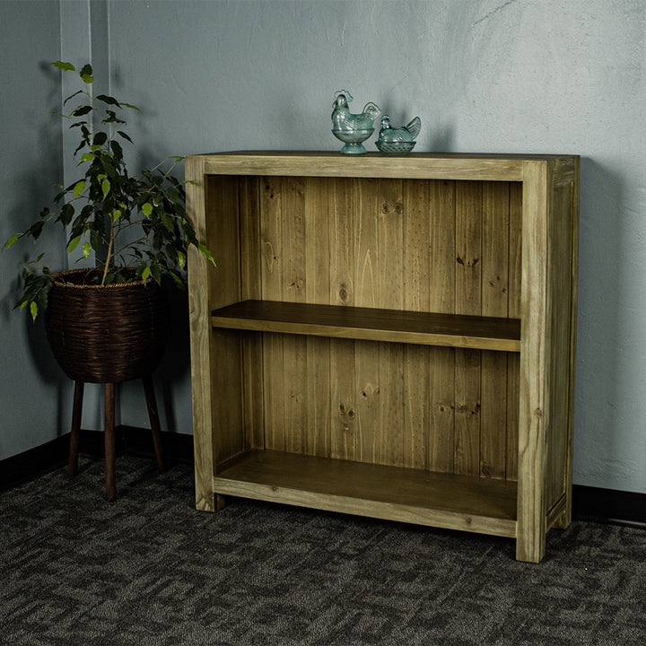 The front of the Vancouver Short Bookcase. There are two blue glass ornaments on top, with a free standing potted plant next to it.