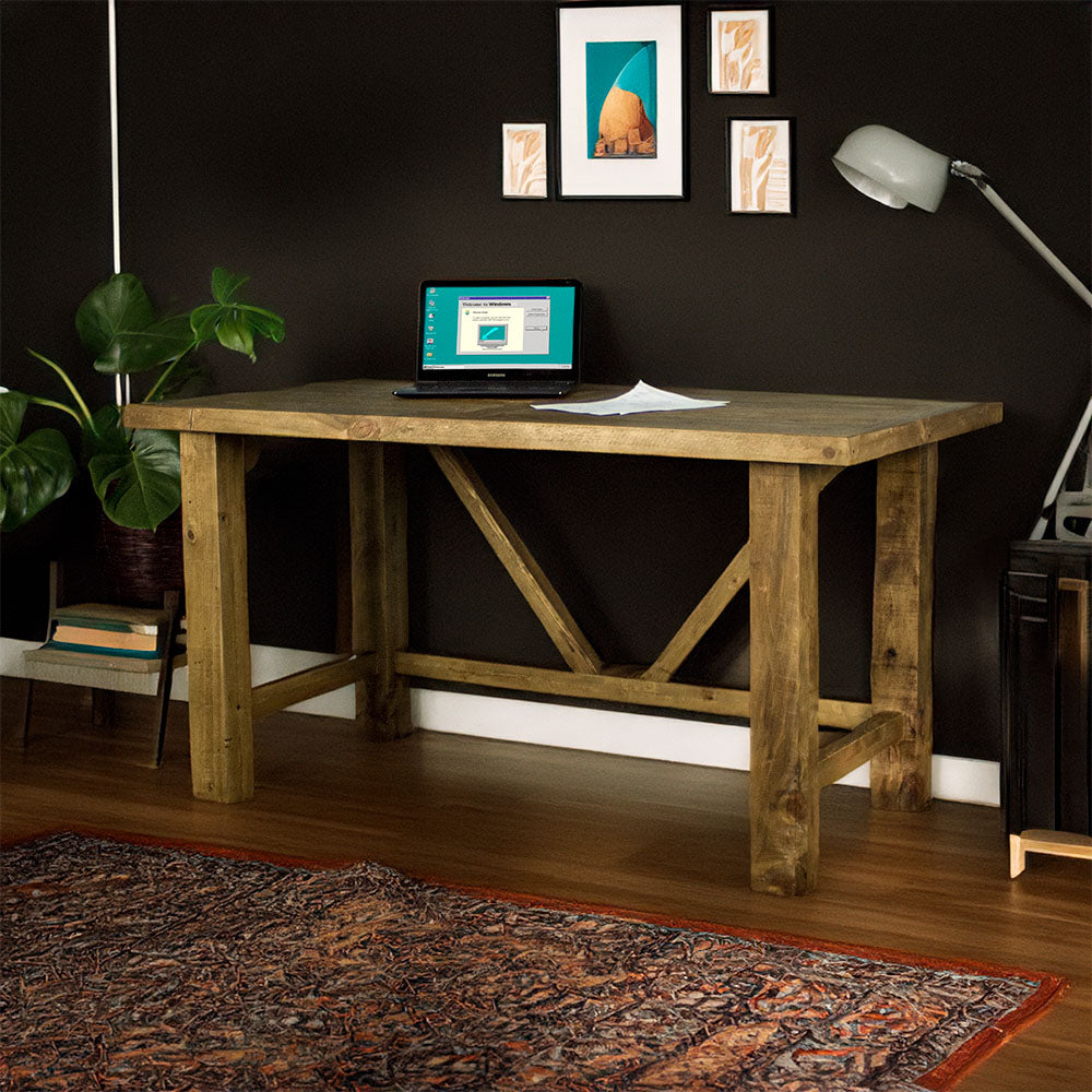 Front view of the Ventura Recycled Pine Desk. There is a laptop and a pile of papers on top. There is a free standing potted plant next to the desk.