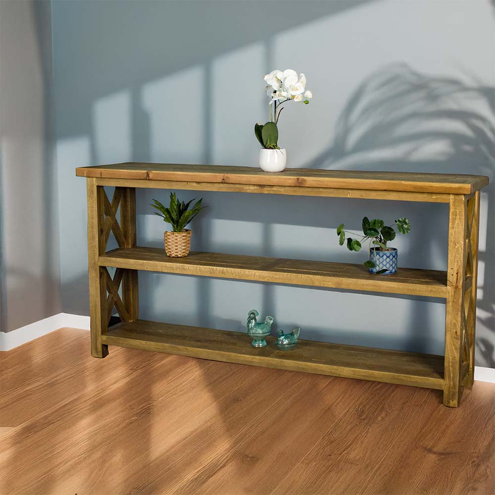 The front of the Ventura Recycled Pine Large Hall Table. There is a pot of white flowers on top. There are two equidistant potted plants on the middle shelf. There are two blue glass ornaments on the bottom shelf.