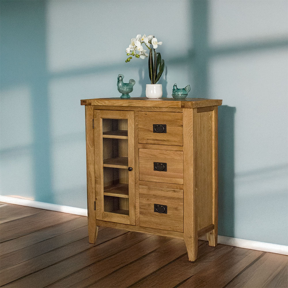 The front of the Yes Compact 1 Door 3 Drawer Oak Buffet. There are two blue glass ornaments and a potted plant on top.