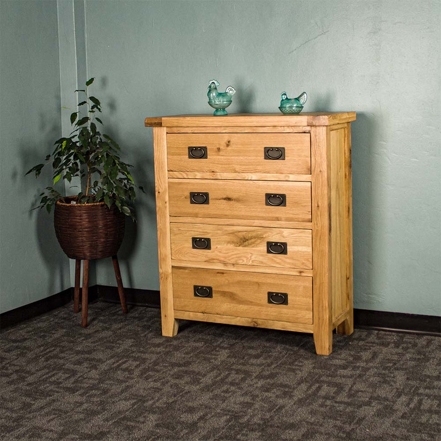 The front of the Yes Four Drawer Oak Tallboy. There are two blue glass ornaments on top and a free standing potted plant next to the tallboy.