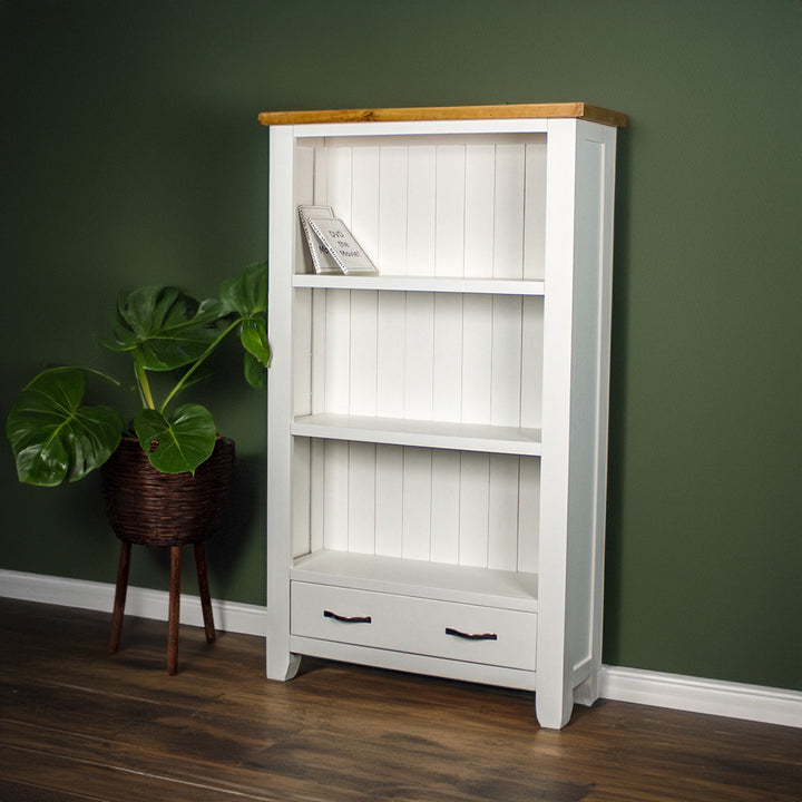 The front of the Felixstowe Pine Bookcase. There are two DVDs on the top shelf. There is a free standing potted plant next to the bookshelf.