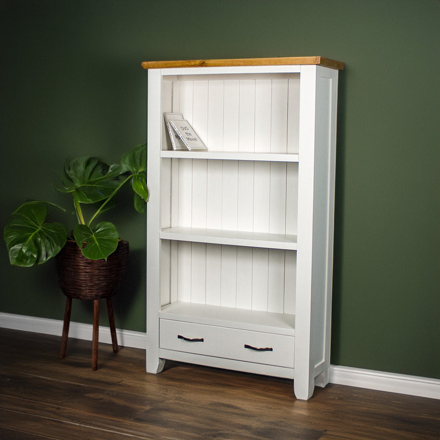 The front of the Felixstowe Pine Bookcase. There are two DVDs on the top shelf. There is a free standing potted plant next to the bookshelf.