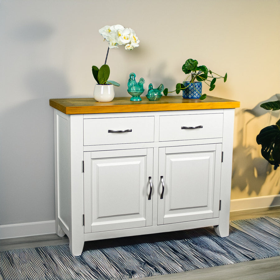 The front of the Felixstowe Small Pine Buffet (White). There are two potted plants with two blue glass ornaments in between on top of the sideboard.