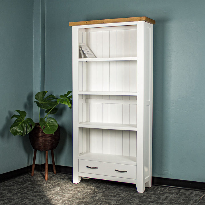 The front of the Felixstowe Large Pine Bookcase. There are two DVDs on the top shelf, and a free standing potted plant next to the bookshelf.