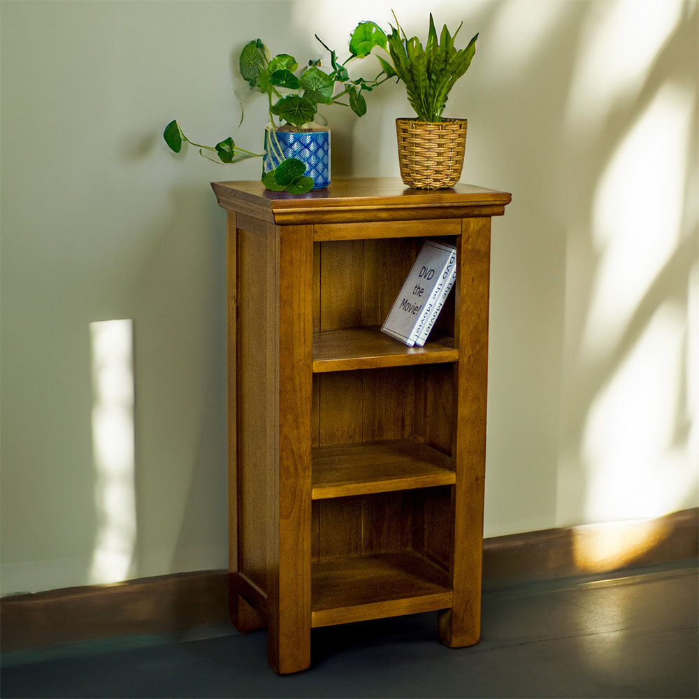 The front of the Montreal Compact Pine Bookcase, with two potted plants on top. There are two DVD cases on the top shelf.