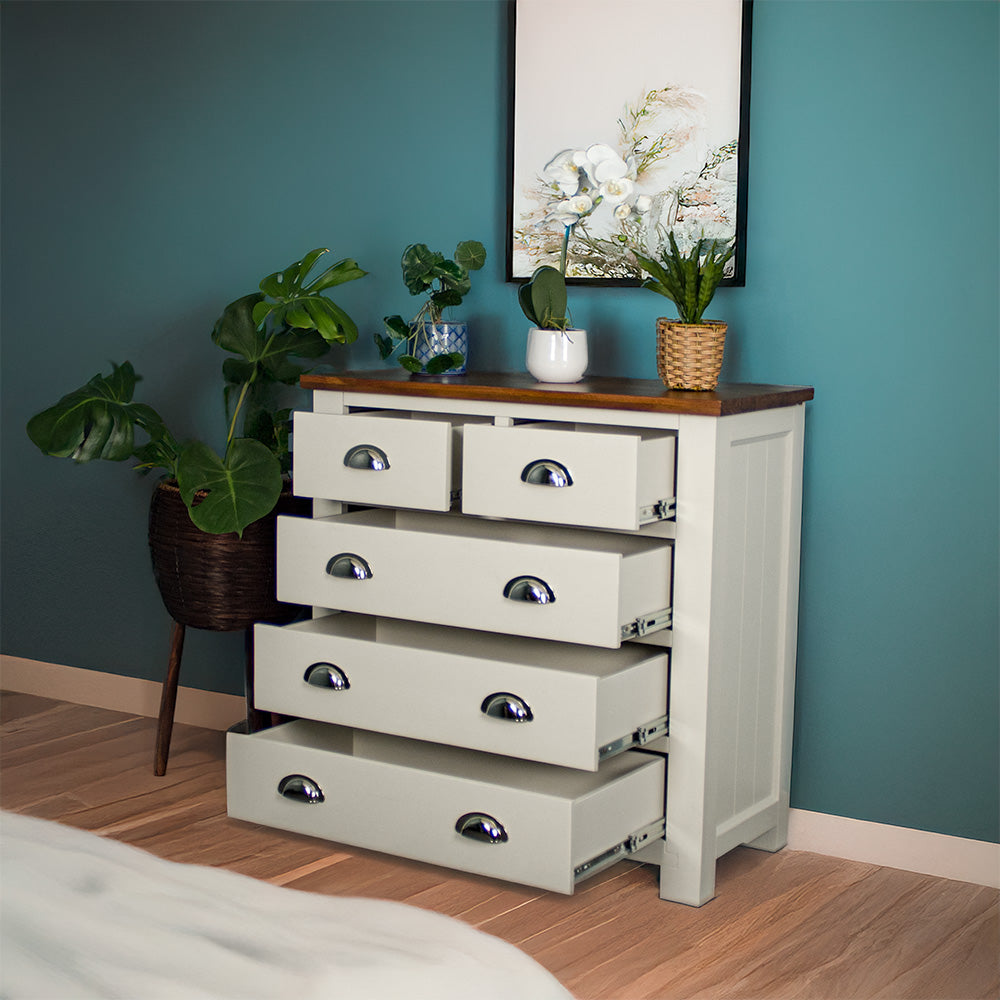 The front of the Alton 5 Drawer Pine Tallboy with its drawers open. There is a free standing potted plant next to it. There are three potted plants on top.