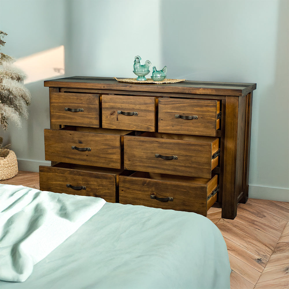 The front of the Botanica Large Seven Drawer Lowboy, with its drawers open. There are two blue glass ornaments on top of a rattan leaf.