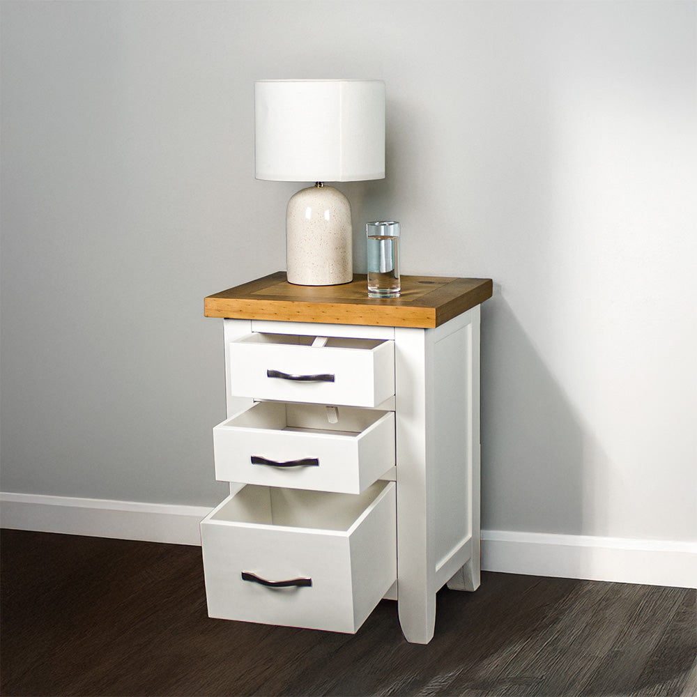 The front of the Felixstowe Pine Bedside Cabinet (White) with its drawers open. There is a lamp and a glass of water on top.