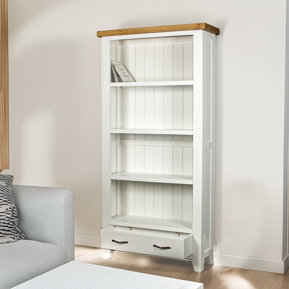 The front of the Felixstowe Large Pine Bookcase with its drawers open. There are two DVDs on the top shelf and a free standing potted plant next to the bookcase.