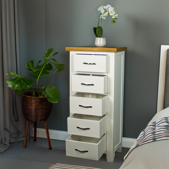 The front of the Felixstowe 5 Drawer Pine Lingerie Chest with its drawers open. There is a small pot of white flowers on top. There is a free standing potted plant next to the unit.