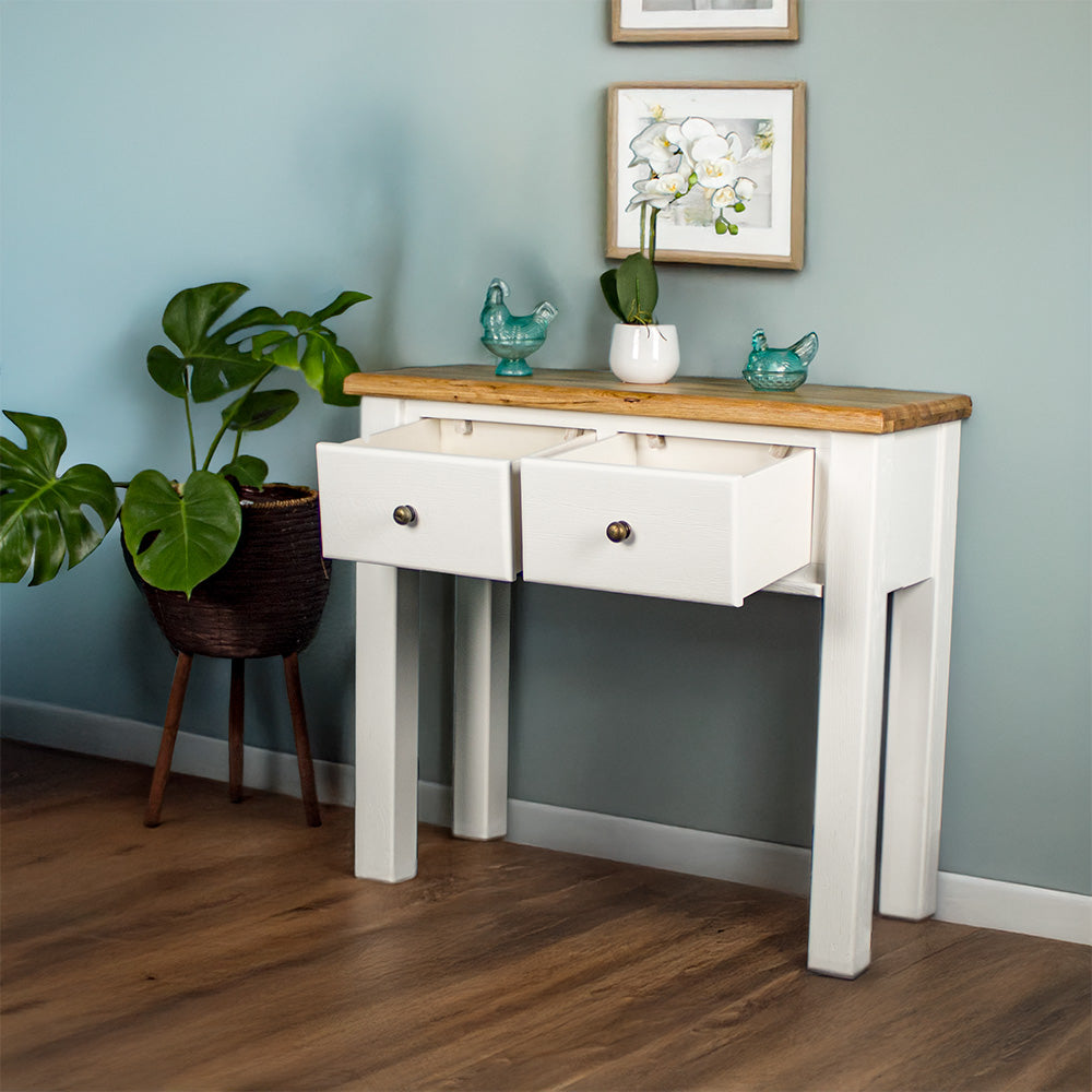 The front of the Loire Oak Hall Table with its drawers open. There are two blue glass ornaments on top with a pot of white flowers in between. There is a free standing potted plant next to the console table.