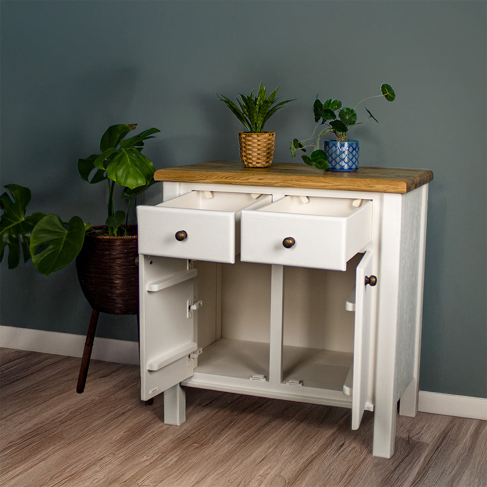 The front of the Loire Small Oak Buffet with its doors and drawers open. There are two potted plants on top with a free standing potted plant next to the sideboard.