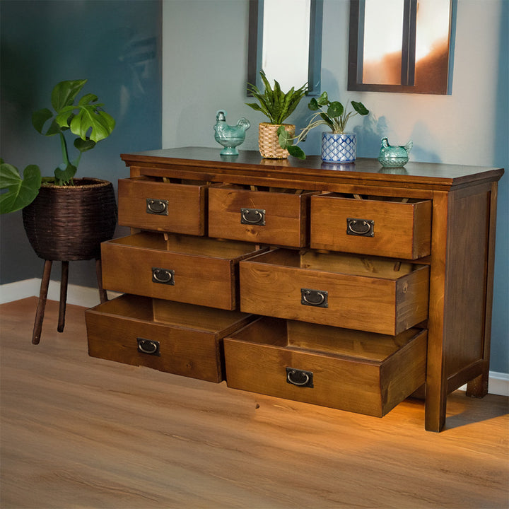 The front of the Montreal 7 Drawer Pine Lowboy with its drawers open. There are two blue glass ornaments on top with two potted plants in between. There is a free standing potted plant next to the lowboy.