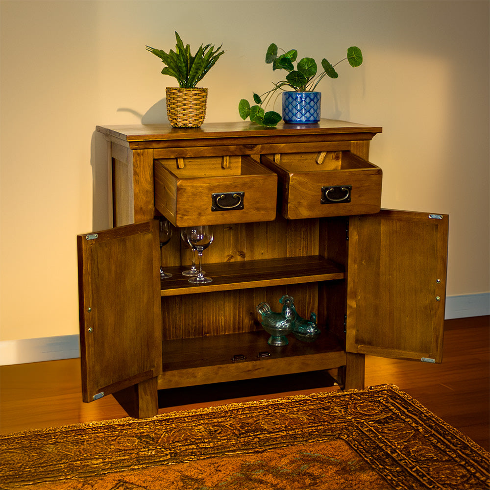 The front of the Montreal Small Pine Buffet with its drawers and doors open. There are two small potted plants on top. There are three wine glasses on the top shelf and two blue glass ornaments on the lower shelf.