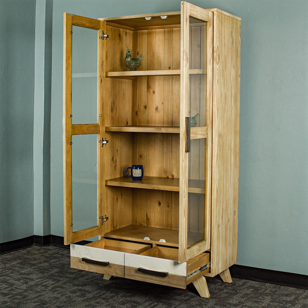 The front of the Soho NZ Pine Display Cabinet with its doors and drawers open. There are two glass ornaments, one on the top shelf, one on the second shelf, and a coffee mug on the third shelf.
