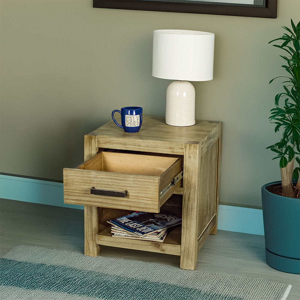 The front of the Vancouver 1 Drawer Lamp Table with its drawer open. There is a lamp and a coffee mug on top. There is a pile of magazines on the shelf underneath.