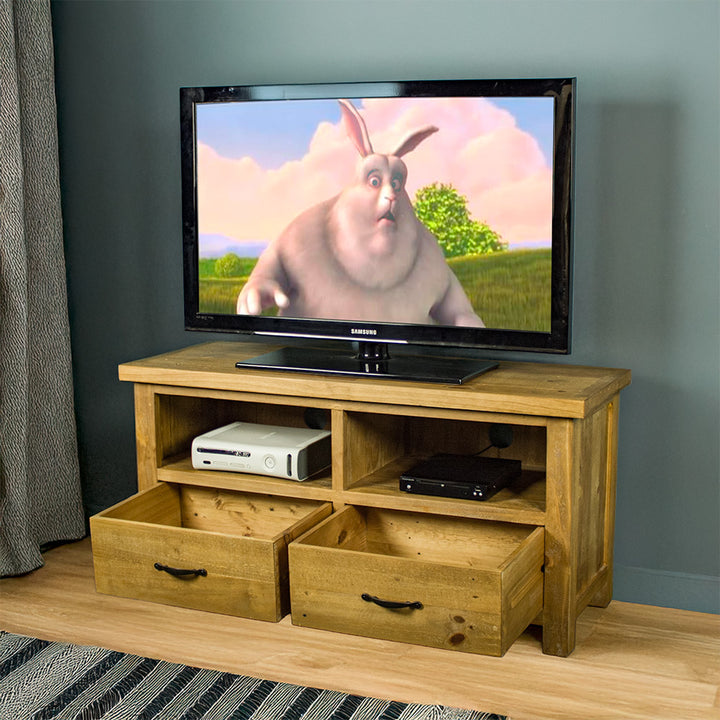 The front of the Ventura Two Drawer Recycled Pine TV Unit, with its drawers open. There is a large TV on top, with a console and DVD player in the shelving below.