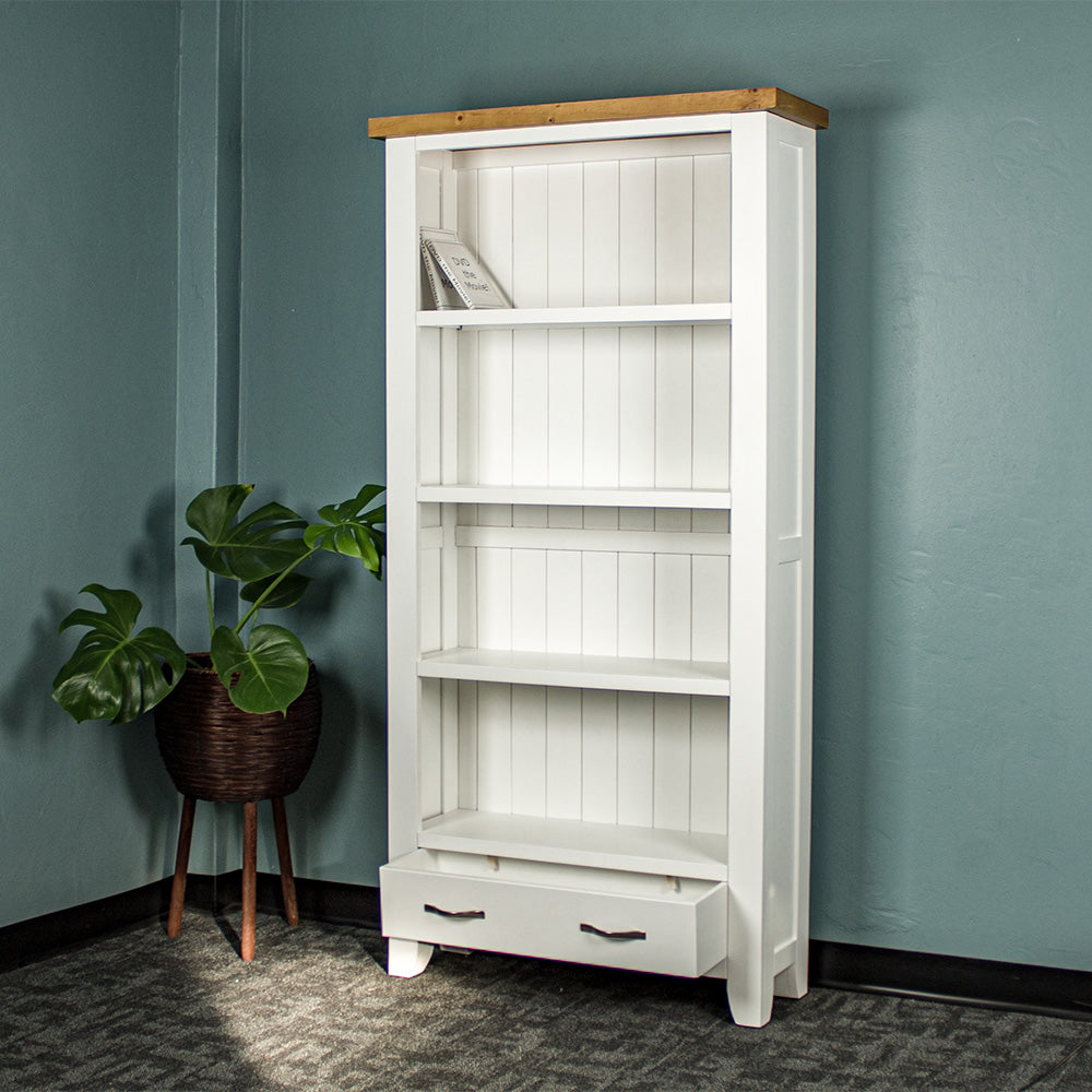 The front of the Felixstowe Large Pine Bookcase with its drawers open. There are two DVDs on the top shelf and a free standing potted plant next to the bookcase.