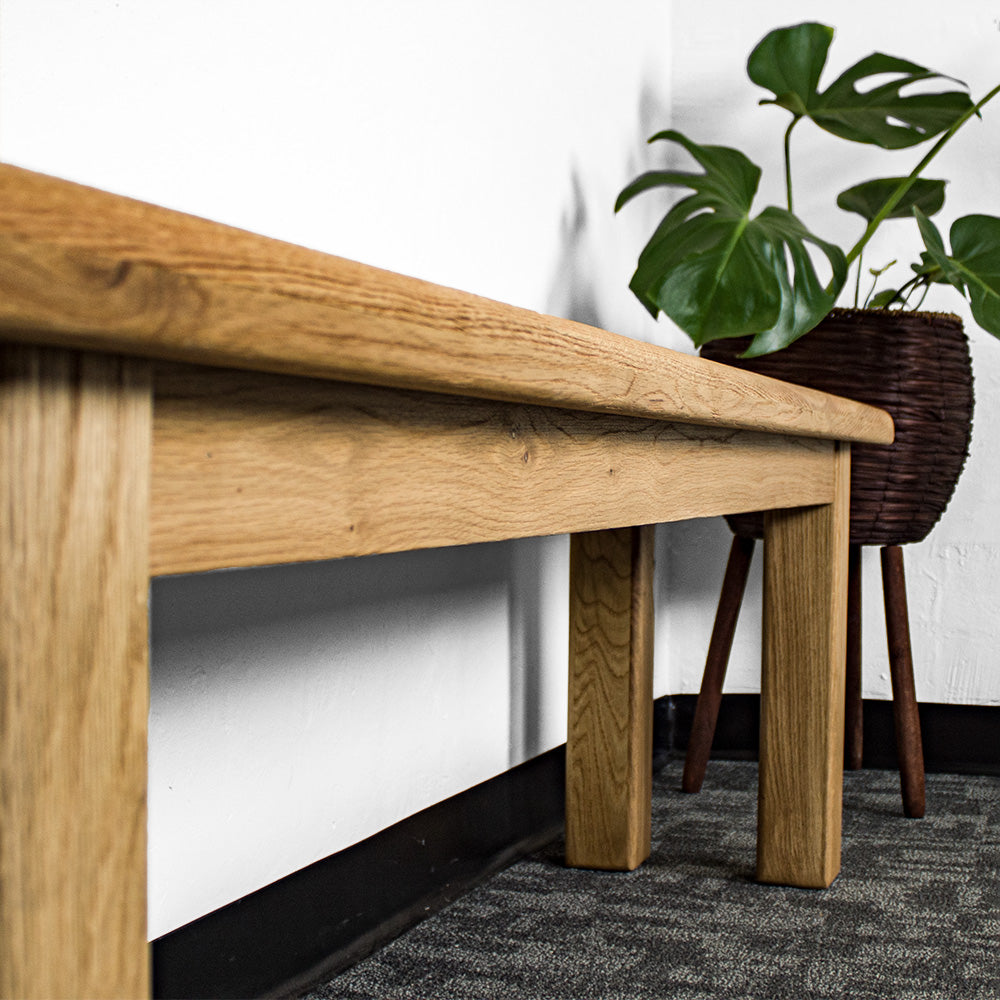 The side of the Loire Solid Oak Bench Seat 1.8m. There is a free standing potted plant in the background.