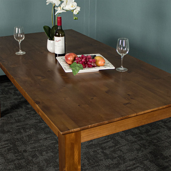 An overall view of the top of the Hamilton Dining Table with Rimu Finish (1.8m), there are two wine glasses, a platter of fruit, a pot of white flowers and a bottle on top of the table.