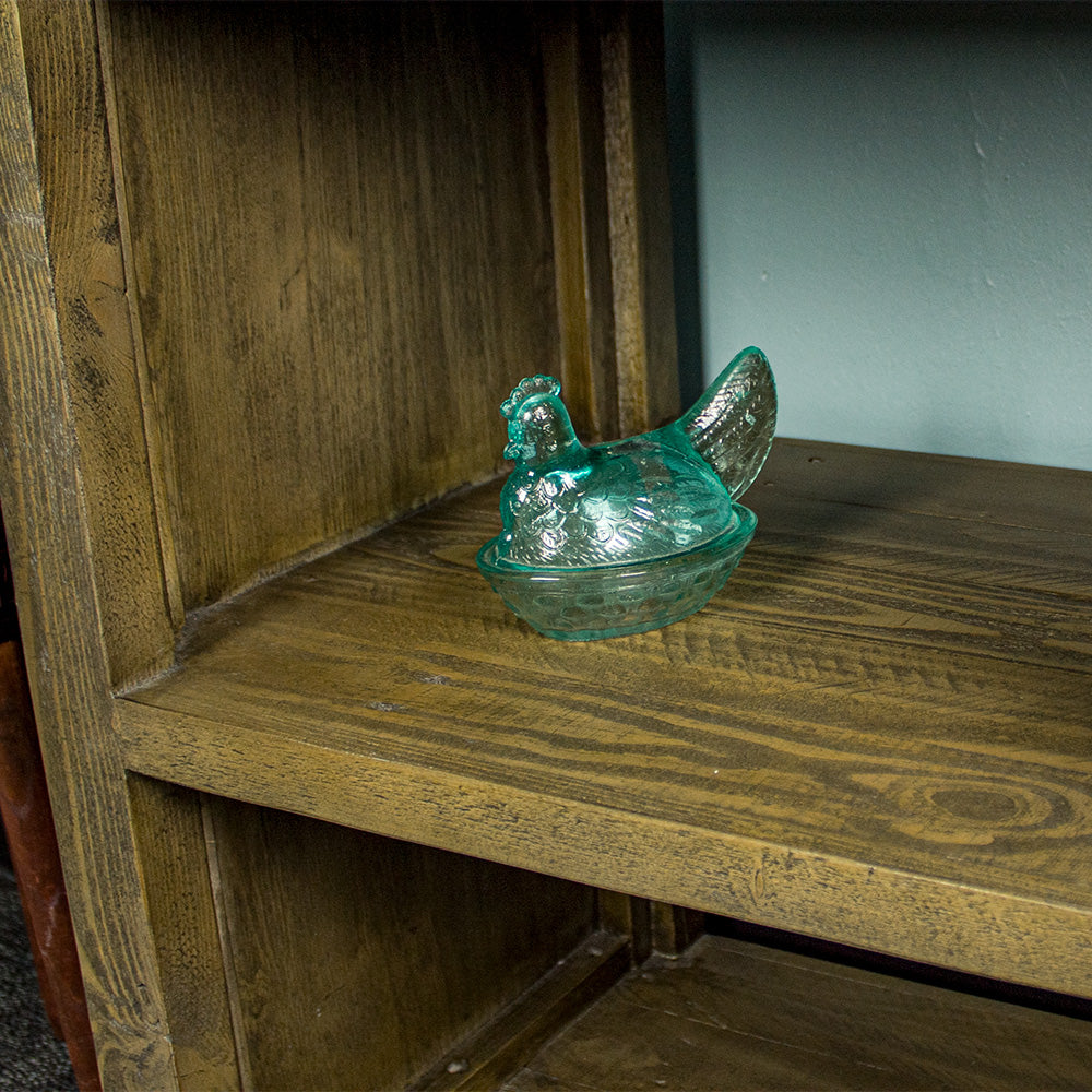 A close up of the middle shelf on the Stonemill Recycled Pine Cube Shelf, there is a blue glass ornament in the shape of a chicken.