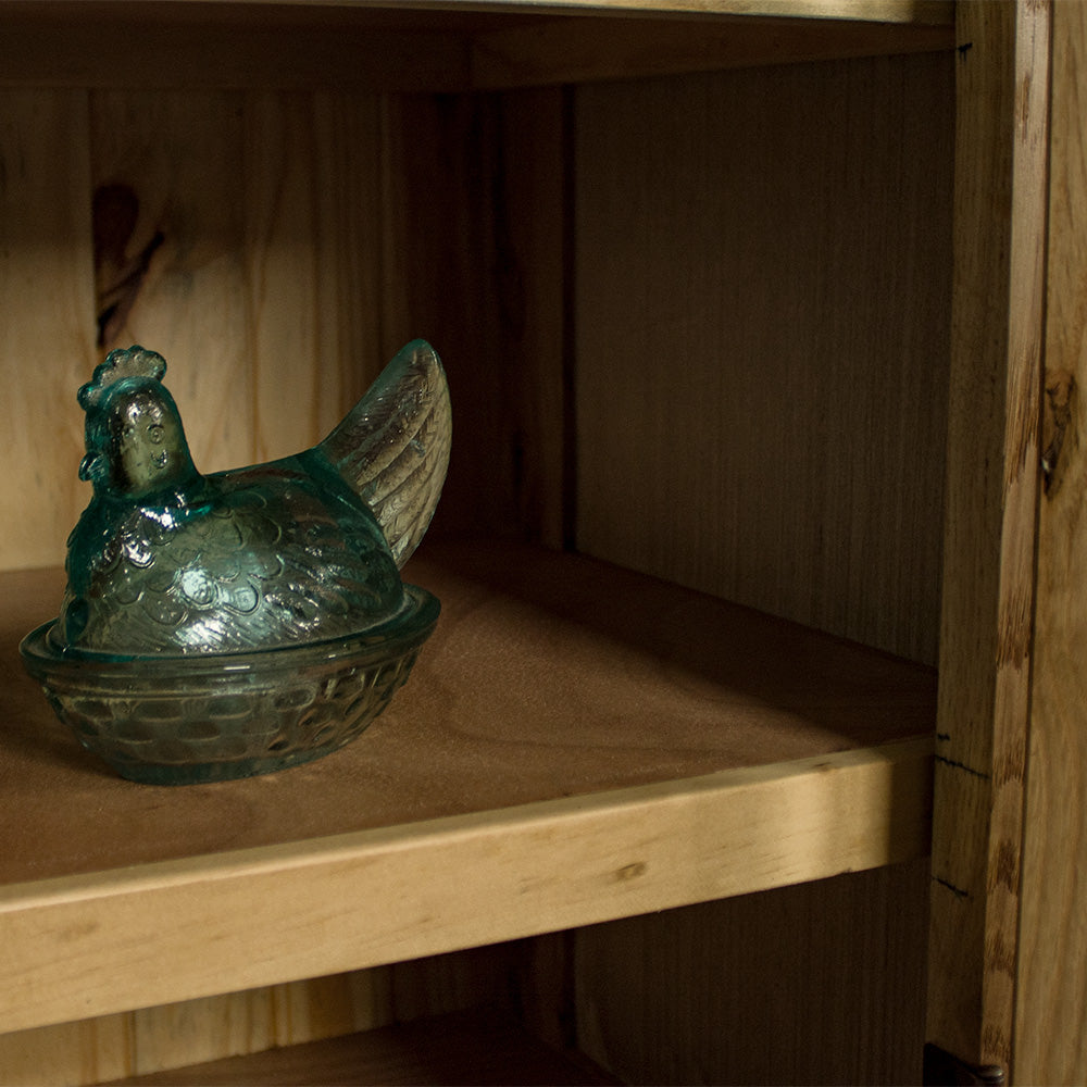 A view of above the shelf on the Yes Oak Display Cabinet. There is a blue glass ornament in the shape of a chicken on the shelf.