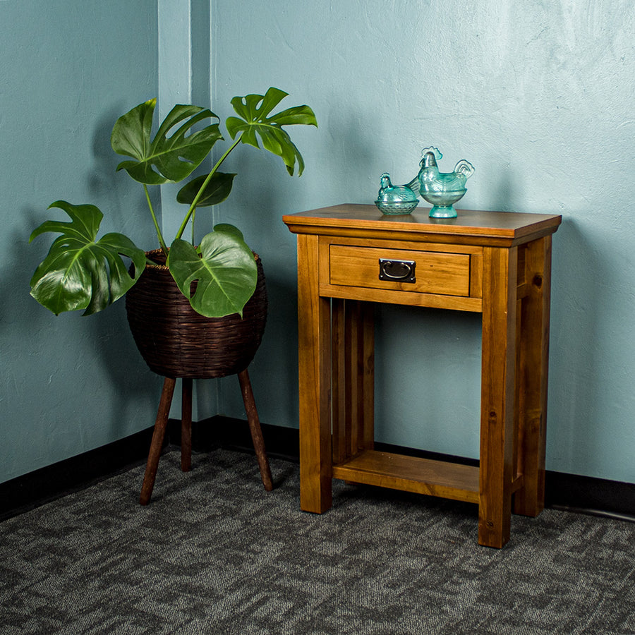 The front of the Montreal Small Pine Hall Table, with two blue glass ornaments on top. There is a free standing potted plant next to it.