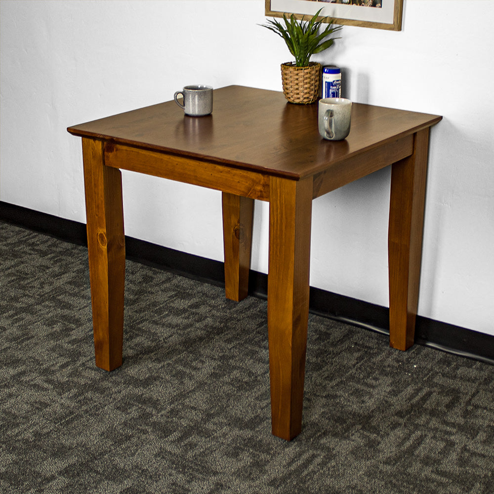 The front of the Hamilton Pine Dining Table (800mm). There is a potted plant, two mugs and a salt shaker on top.