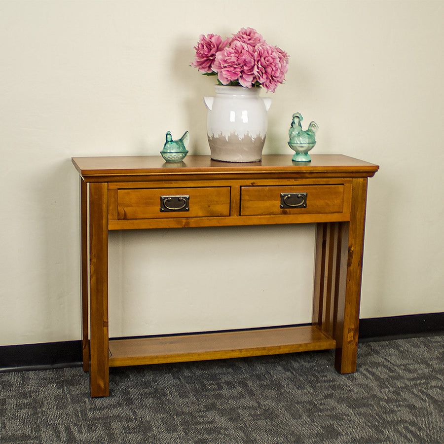 The front of the Montreal Pine Hall Table. There is a large vase with pink flowers in between two blue glass ornaments.