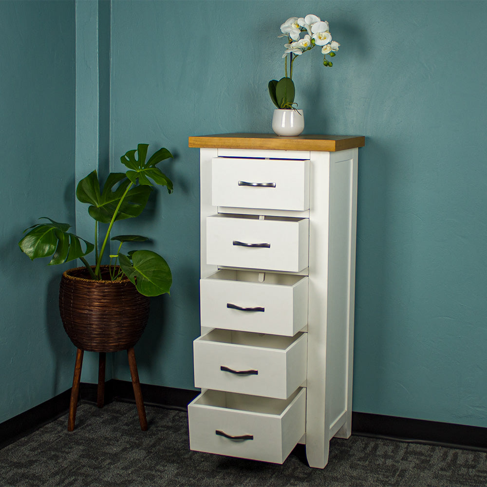 The front of the Felixstowe 5 Drawer Pine Lingerie Chest with its drawers open. There is a small pot of white flowers on top. There is a free standing potted plant next to the unit.